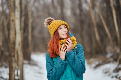 白天，穿着蓝色夹克和棕色针织帽的女人站在雪地上
